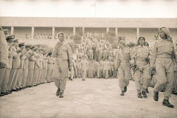 Group of men descending a staircase with military escort. The path is lined with men in military uniform applauding.