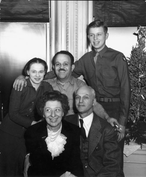 Informal portrait of Dickey Chapelle (back left), her husband Tony Chapelle (back center), her brother Bob Meyer (back right), and her parents Paul Meyer and Edna Engelhardt Meyer. There is a small Christmas tree in the background on the right.