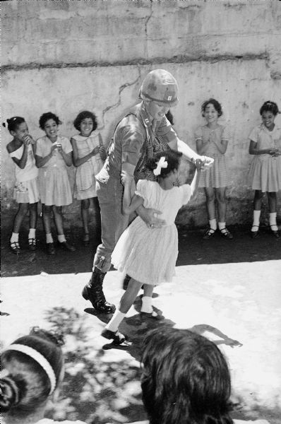 Paratroop Captain E.F. McGushin, Commander of Co. C, dancing with a 4th grade girl at recess in Santo Domingo, Dominican Republic.