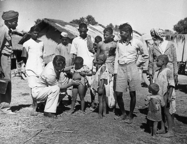 Dr. P.C. Issaris of Greece examines the spleen of a child in India. Men and other children stand around them watching.
