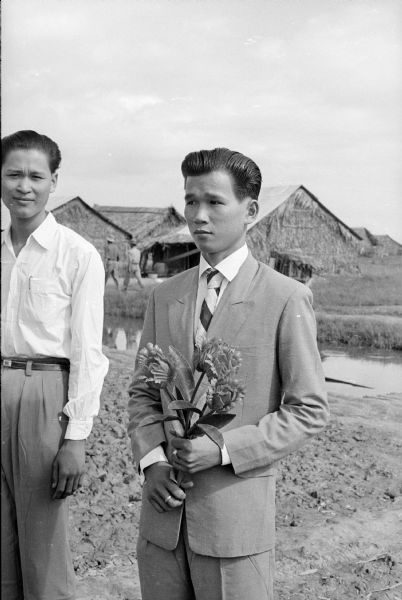 Tien Vinh Le on his wedding day in the village of Binh Hung, Vietnam. He wears a suit and tie, and holds a bouquet of flowers. 
