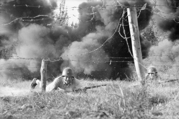 Chinese National marine crawls on his stomach beneath barbed wire in an infiltration training course in Formosa. Another man is on the right. The course includes live machine gun fire and mortar fire.