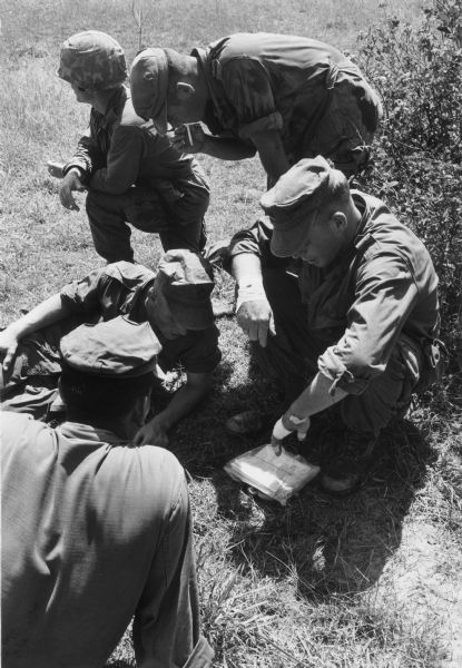 View of five soldiers in Vietnam, some of whom are reading a map, and others smoking cigarettes.