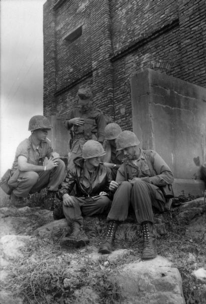 A group of U.S. soldiers seated near a brick building in Vietnam consulting a map.