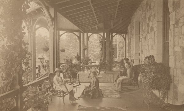 Group of people posed on a large porch at Snug Harbor, including: Helen Sturges holding a tennis racket, Clara Sturges, unidentified person (possibly a visiting cousin), Mary Delafield (Mrs. George Sturges (with hat), Wallace Delafield Sturges, Rosalie Sturges (on porch railing), Lida Ramsey, and Elizabeth Ayer (with high hat, later married Frank Johnson).