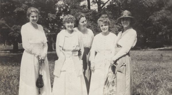 Outdoor informal group portrait of four women standing together at Lake Geneva. Trees are in the background.