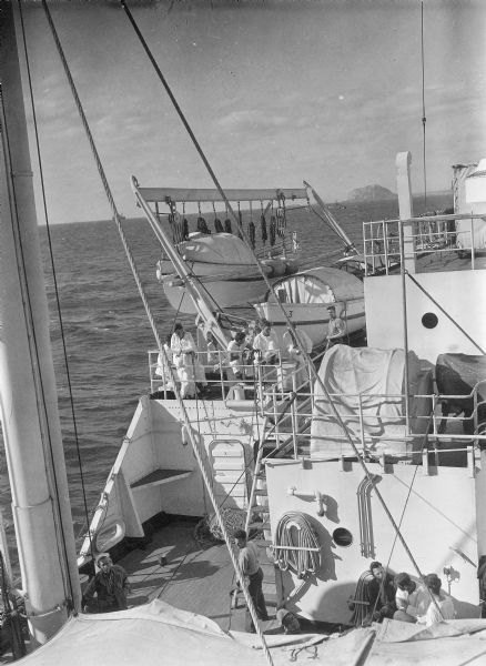 View from the deck of the hospital ship, the USS <i>Samaritan</i>, at sea. There are other ships and a shoreline in the background.