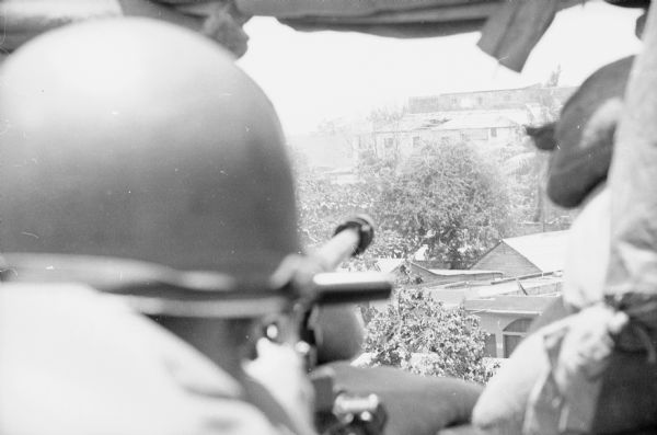 View over the shoulder of a soldier of the 82nd Airborne firing a .50 machine gun out a high window of Observation Post #1 in Santo Domingo, Dominican Republic.