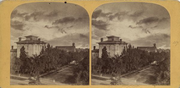 Elevated stereograph of the William H. Metcalf residence at the corner of Cass Street and Juneau Avenue. Trees line the street and sidewalk along the perimeter of the property.