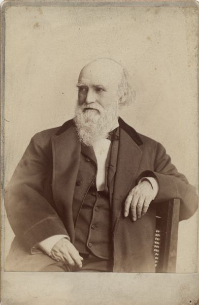 Waist-up studio portrait of William Metcalf seated sideways in a chair.
