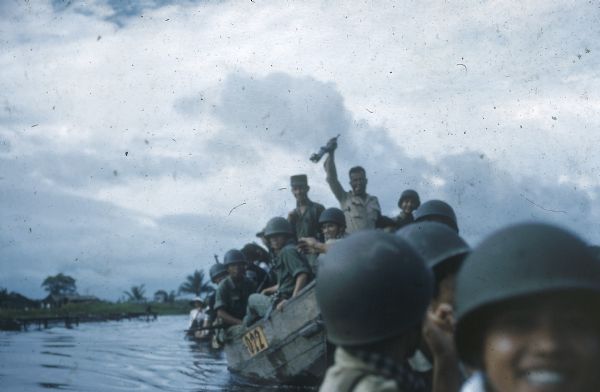 View from water of a newly formed company of Vietnamese Sea Swallows riding in a boat near Binh Hung as they joyously celebrate its graduation from training by starting out on its first military mission. The mission is to guard Father Hoa while he says mass at Tan Hung Tay.