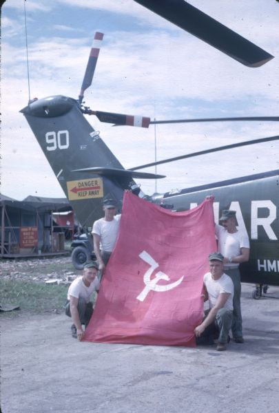 U.S. Marines posing with a captured Russian flag in front of a helicopter at the Soc Trang U.S. Marine helicopter base in Vietnam.