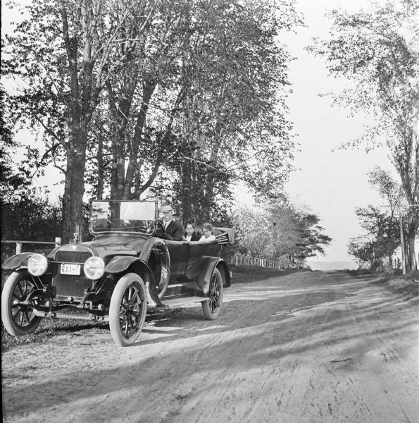 Family of four seated in a Hudson automobile parked on the side of a tree-lined country road.