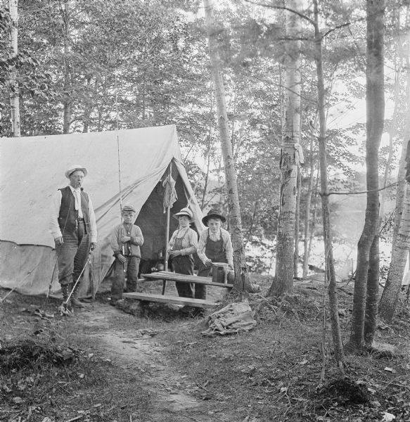 Dr. Smith's brother-in-      law, Franklin E. Bump, and three of his children, Franklin E. Jr., Warner, and Millard Bump, standing in front of a tent in the woods near a lake. They are all holding fishing poles or fishing equipment.