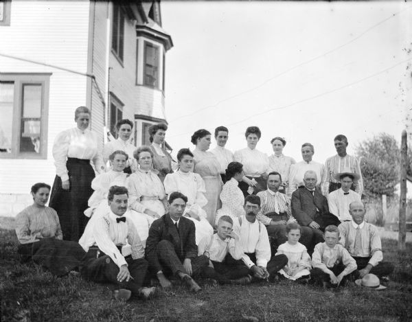 Dr. Joseph Smith's family grouped together in an outdoor portrait in front of a house.  Mary Smith is standing in the back row third from the right.