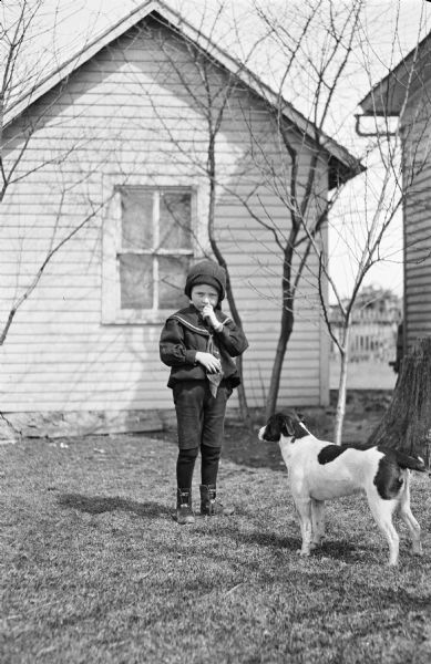 A boy standing in a yard with a dog.