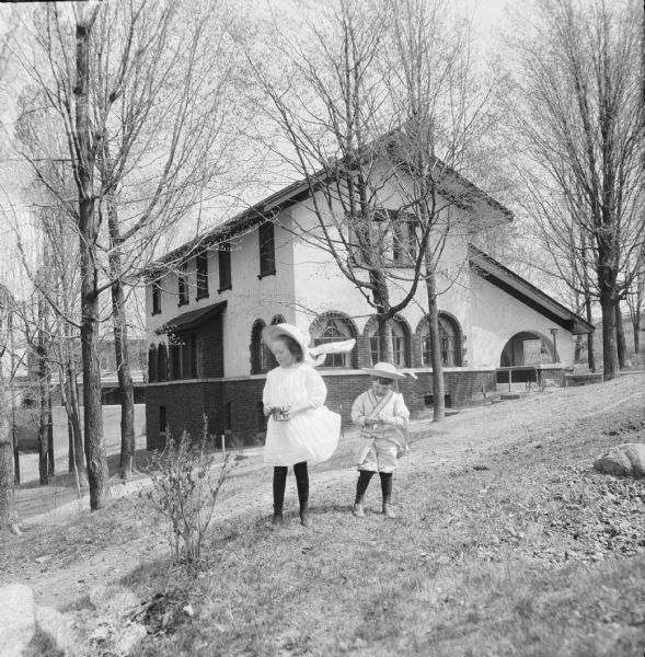 Two children outside near the driveway of a house. A bicycle can be seen in the background.