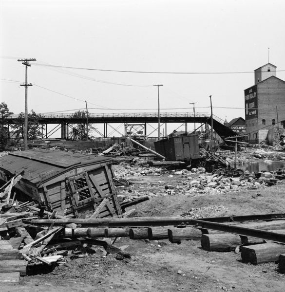 Aftermath of a flood. Debris of railroad ties, tracks, and cars are scattered beneath a bridge.