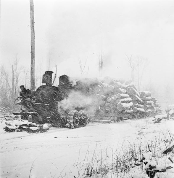 A steamhauler pulling logs on skids to the mill during a snowstorm.