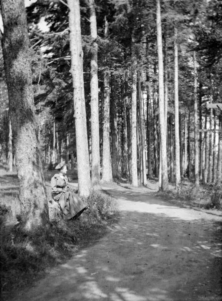 Mary E. Smith sitting on the edge of a trail within a forest of pine trees in Canada.