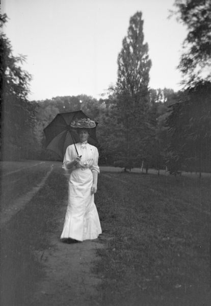 Mary E. Smith walking along a path in a park in Vienna, Austria holding an umbrella.