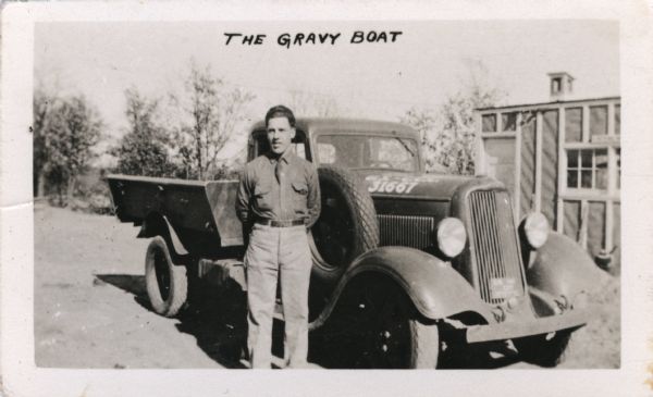 A man in a uniform stands beside a Civilian Conservation Corps (CCC) truck. The photograph is annotated as: "The Gravy Boat." There is a building in the background on the right.