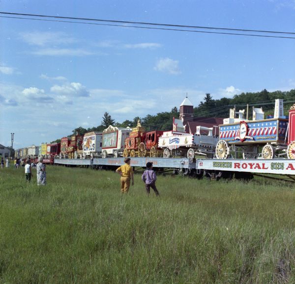 View of local residents standing in the grass watching the Circus World Museum Train pass through Elroy and Union Center. The train, which did not normally pass through the area, was rerouted after a derailment in the Grafton area. The photograph appeared in the Hillsboro <i>Sentry Enterprise</i>.