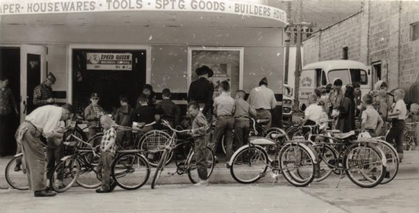 View from street of group of local boys taking part in a celebration of National Bicycle Week. Members of the Shaker-Callaway Post of the VFW were on hand to place strips of Scotch Lite on the boys' bicycles and are also pictured. Sterling Standiford, a State Trooper, was also present to explain proper operation of bicycles on streets and highways. The activities took place outside of Sherman Hardware.