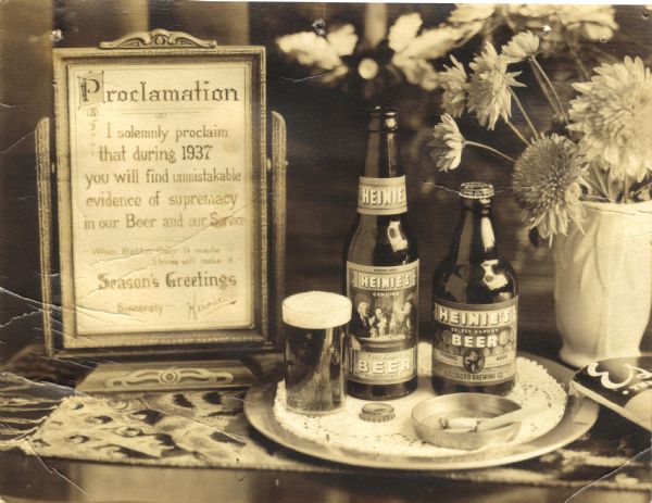 Display of a glass of beer, and a bottle of Heinie's Old Lager Beer bottle, and a bottle of Heinie's Strong Beer. There are cigarettes in an ashtray, flowers in a vase, a copy of <i>Esquire</i> magazine, and a framed "Proclamation." From 1936 to 1939, Heinie's Beer was brewed in Hillsboro as the Hutter Brewing Company, the owner of Hillsboro Brewery, had leased out the brewery to George Heinrich. In 1939, the brewery closed, reopened, and began to produce Hillsboro Pale beer once again.