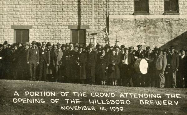 Outdoor group portrait of portion of the crowd attending the Reopening of the Hillsboro Brewery by C.H. Pfeiffer. Members of the band stand in the background holding their instruments above their head.
