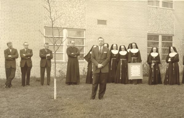Dr. Thomas Boston and unidentified group standing outdoors on the lawn in front of a building (most likely St. Joseph's Hospital employees and State Medical Society members). Boston worked at St. Joseph's Memorial Hospital for several years, and is shown here with the Community Achievement Award from the State Medical Society.