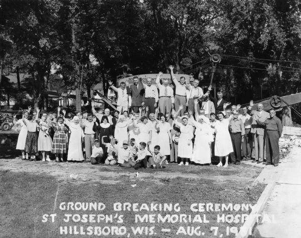 Slightly elevated group portrait of people posed on and around a crane and waving at the groundbreaking ceremony for St. Joseph's Memorial Hospital.