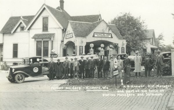 View across street towards group of men standing on the sidewalk in front of the Perfect Oil Corporation in front of a Mobiloil truck. They are the station managers and salesmen, and H.R. Knower, the branch manager, is indicated with an arrow. Perfect Oil was active in Hillsboro from 1927 to the early 1940's.
