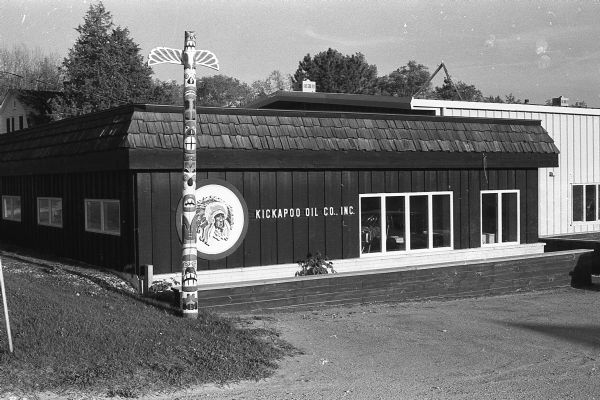 Exterior view of the Kickapoo Oil Company's corporate offices. A carved wood totem pole stands in front of the building. Headquartered in Hillsboro, the company was started in 1958 by Raymond Knower. Kickapoo is credited with having the first self-service stations as Knower had to convince the Wisconsin State Legislature to change the law to allow people to pump their own gasoline. Kickapoo Oil owned over 60 stations before it was sold to Kwik Trip in 1988.