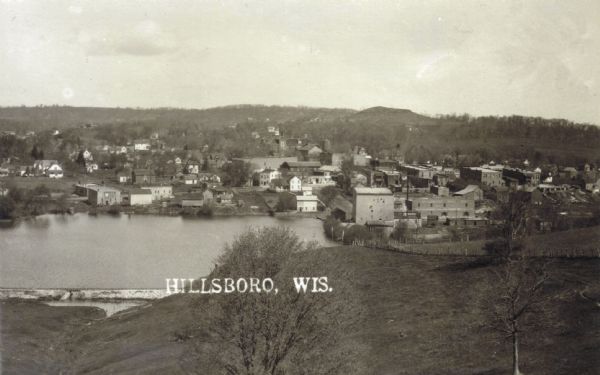 Elevated view of the town of Hillsboro and Field Veterans Memorial Lake. There are buildings, houses, hills, and trees. The Hillsboro Mill is on the right side of the lake.