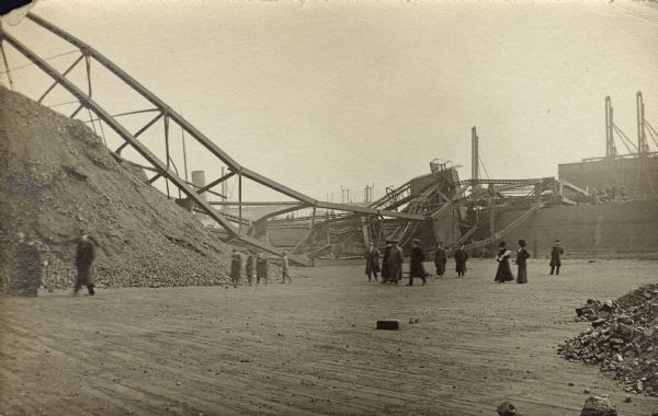 Men and women walking around piles of coal while examining a collapsed structure in a coal yard.