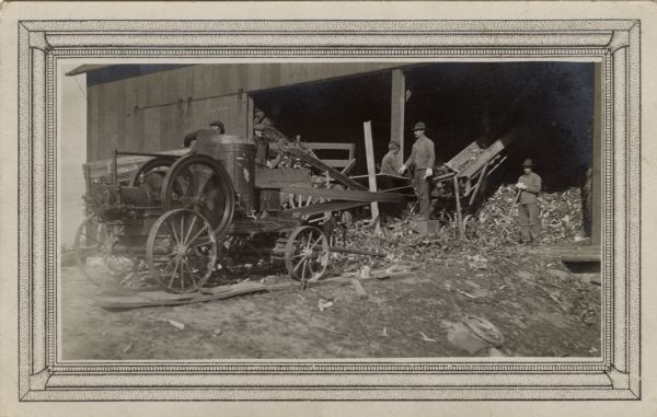 An early wood chipper with belts and a steam engine is closely watched by the William Fiebelkorn farm workers. The postcard is addressed to Anna Fiebelkorn by her sister Ida.