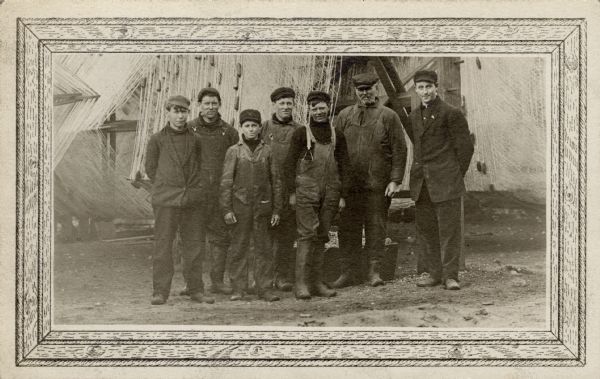 Fishermen from the <i>Frank Braeger</i> fishing tugboat are standing for a group portrait in front of their fishing nets on Jones Island.