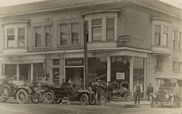 The First Ave Auto Garage, which seems to be an auto sales showroom, at 509 First Avenue in the S. Sixth Street neighborhood of Walker's Point is featured in this photograph. There are a number of automobiles on the street and even on the sidewalk with men sitting in the cars and pausing on the street to view them. Above the Auto Garage is the office of Dr. Johnson, Physician and Surgeon. Next door is Jac Lemmer's Place, a 'Sample Room'. The sidewalk is paved, the street is dirt, and there are streetcar rails in the lower right corner.