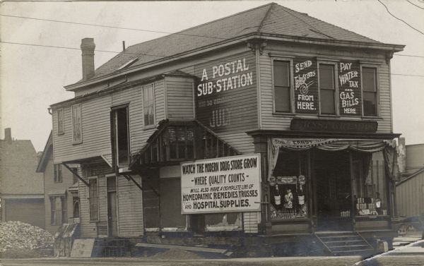 View the from the street of a building being remodeled to accommodate two businesses: a drugstore on the ground floor and a postal sub-station on the second floor. The drugstore at 508 First Avenue, bought by Ernst Krembs in 1908, has a large billboard that says "Watch the Modern Drug Store Grow, Where Quality Counts, Will Also Have a Complete Line of Homeopathic Remedies, Trusses and Medical Supplies." In the window there is a display for the Pabst Extract, "For Perfect Health from Childhood to Old Age." The second floor postal sub-station has two signs. One says "Send Telegrams from Here," the other says "Pay Water, Tax and Gas Bills Here." The side of the building announces that the sub-station will be established July 1.