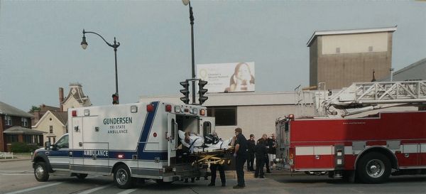 Gundersen Tri-State ambulance and fire truck personnel rescue a man who may have had a seizure at the Bimbo Bakery. The vehicles are parked in the street, light posts and traffic lights are behind the ambulance.