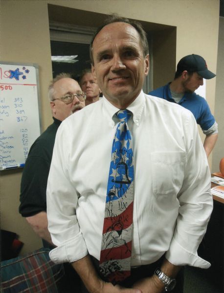 La Crosse Loggers baseball team owner Dan Kapanke, at a Republican Election Rally at La Crosse County Republican Headquarters. He is a former Wisconsin State Senator who lost to Jennifer Schilling in the 2011 recall elections. He is wearing a patriotic necktie with stars and stripes, the Statue of Liberty, Liberty Bell and "We the People" decorating it. Several other men stand behind him.

