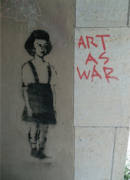 Graffiti on the wall next to the doorway of the Hollywood Theatre. On the left is a stenciled image of a girl wearing a jumper and on the right is the text: "Art As War."