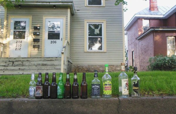 Empty booze bottles lined up on a concrete wall in front of an apartment on 8th Street. Among the labels are, "Michelob Golden Light," "Rolling Rock Beer," "Jack Daniels Tennessee Whiskey," "Mr. Boston Sour Apple," "Captain Morgan Spiced Rum" and "American Honey."