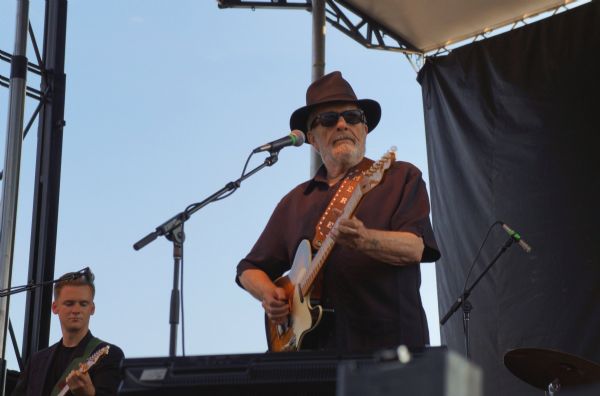 Merle Haggard on guitar at the Southside Oktoberfest Grounds. He is wearing a hat and sunglasses. Another guitarist is on the left.