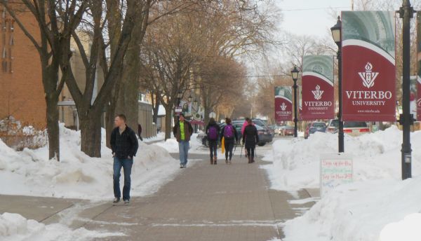 Students walking on the Viterbo University campus in winter. Viterbo University is a Roman Catholic liberal arts university. On the right are banners, on the left, campus buildings. Snow covers the ground.