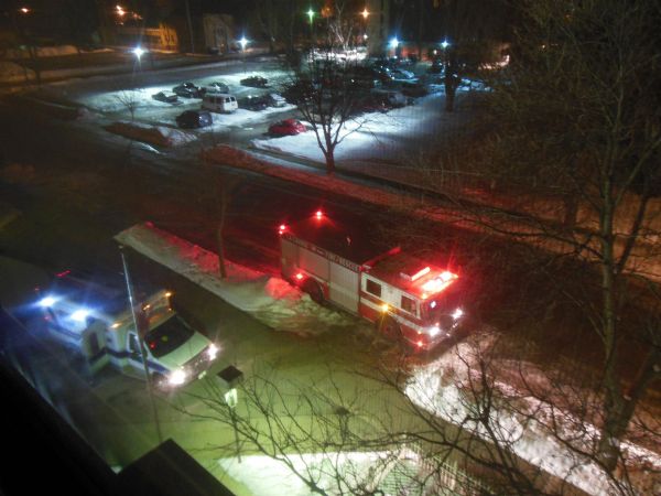 Elevated view of fire and ambulance vehicles after dark at Becker Plaza. In the background is a parking lot. Snow is on the ground.