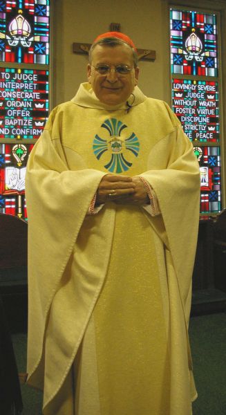 The Cardinal Raymond Burke, then head of the Vatican Supreme Court, posing for a portrait in Bishop’s Vestry, Saint Joseph the Workman Cathedral. He is wearing a gold chasuble (robe) with embroidery on the chest, and red zucchetto (cap). This was on the day of a Mass of Thanksgiving in his home diocese soon after Ray Burke was made a cardinal. In the background are two stained glass windows. A crucifix is partially hidden by the Cardinal's head.