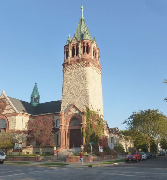 View across street of the Christ Episcopal Church main tower at the corner of 9th & Main Streets. A man is walking along the sidewalk and automobiles are parked at the curb.