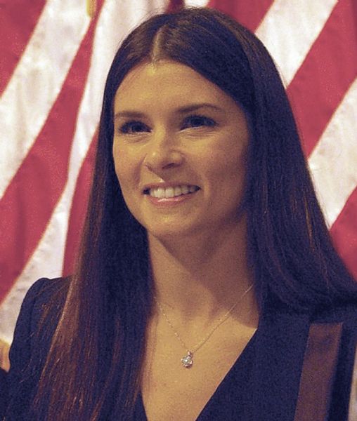 Head and shoulders portrait of Danica Patrick, the most successful woman in American open-wheel racing. After 2010 she made the switch from IndyCar racing to Stock Car racing. She is posing in front of an American flag.